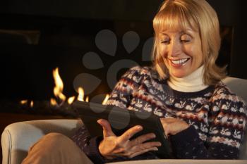 Mature woman using tablet in front of fire at home