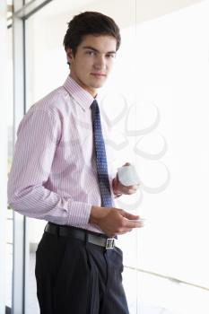 Young Businessman Standing In Corridor Of Modern Office Building Drinking Coffee