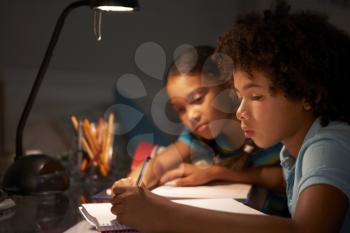 Two Children Studying At Desk In Bedroom In Evening
