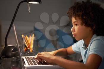 Young Boy Studying At Desk In Bedroom In Evening On Laptop