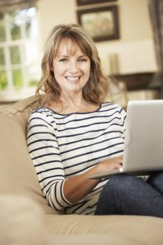 Mature Woman Sitting On Sofa At Home Using Laptop