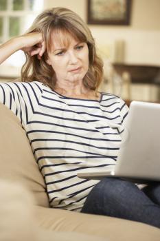 Puzzled Mature Woman Sitting On Sofa At Home Using Laptop