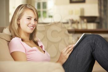 Teenage Girl Sitting On Sofa At Home Using Tablet Computer