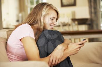 Teenage Girl Sitting On Sofa At Home Texting On Mobile Phone