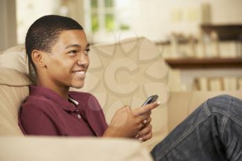 Teenage Boy Sitting On Sofa At Home Texting On Mobile Phone