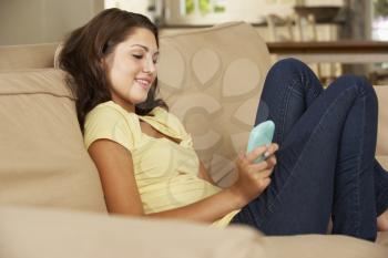 Teenage Girl Sitting On Sofa At Home Texting On Mobile Phone
