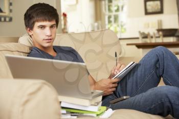 Teenage Boy Sitting On Sofa At Home Doing Homework Using Laptop Computer