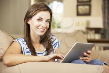 Woman Sitting On Sofa At Home Using Tablet Computer
