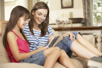 Mother And Daughter Sitting On Sofa At Home Using Tablet Computer