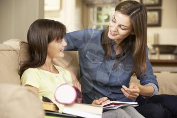 Mother Helping Daughter With Homework Sitting On Sofa At Home