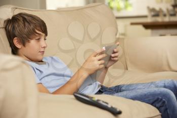 Young Boy Sitting On Sofa At Home Using Tablet Computer