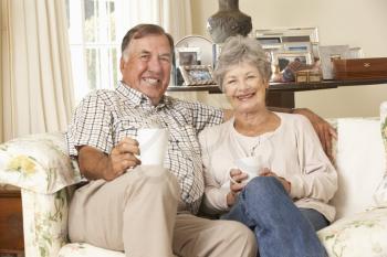 Retired Senior Couple Sitting On Sofa Drinking Tea At Home Together