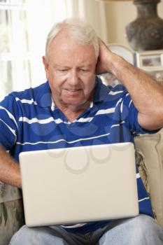 Frustrated Retired Senior Man Sitting On Sofa At Home Using Laptop