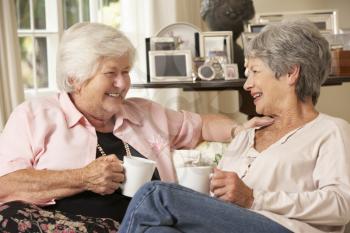 Two Retired Senior Female Friends Sitting On Sofa Drinking Tea At Home