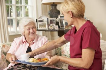 Helper Serving Senior Woman With Meal In Care Home