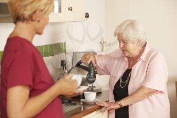 Home Help Sharing Cup Of Tea With Senior Woman In Kitchen