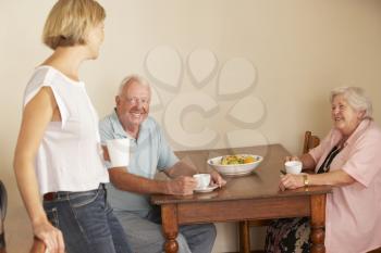 Adult Daughter Sharing Cup Of Tea With Senior Parents In Kitchen