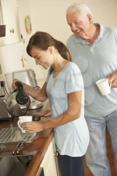Teenage Granddaughter Sharing Cup Of Tea With Grandfather In Kitchen