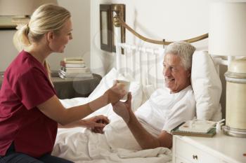 Health Visitor Giving Senior Male Hot Drink In Bed At Home