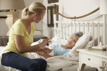 Adult Daughter Giving Senior Female Parent Medication In Bed At Home