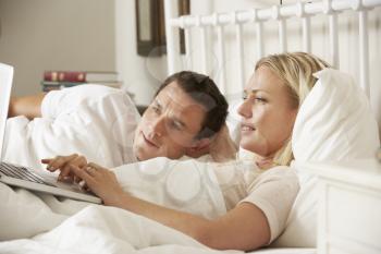 Couple Using Laptop In Bed At Home