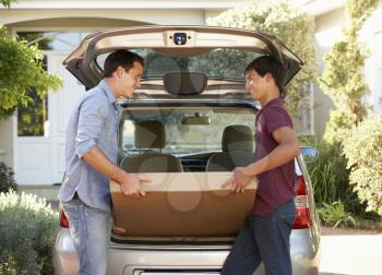 Father And Teenage Son Loading Large Package Into Back Of Car