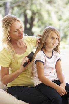 Mother Brushing Daughters Hair On Sofa At Home