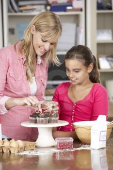Mother And Daughter Decorating Homemade Cupcakes In Kitchen