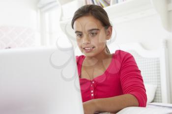 Girl Doing Homework At Desk In Bedroom Using Laptop
