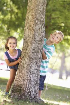 Two Children Hiding Behind Tree In Park