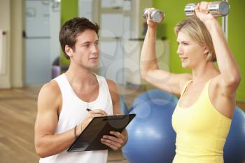 Woman Exercising Being Encouraged By Personal Trainer In Gym