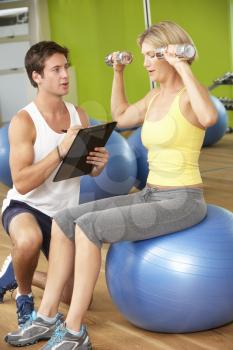Woman Exercising Being Encouraged By Personal Trainer In Gym