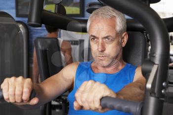 Middle Aged Man Using Weights Machine In Gym