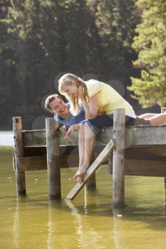 Romantic Couple Sitting On Wooden Jetty Looking Out Over Lake
