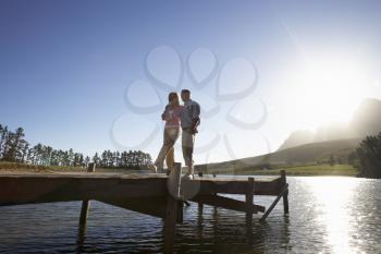 Senior Couple Standing On Wooden Jetty Looking Out Over Lake