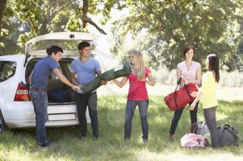 Group Of Young Friends Unloading Camping Equipment From Trunk Of Car