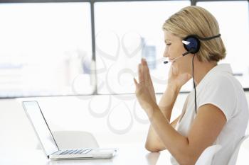 Businesswoman Sitting At Desk In Office Using Laptop Wearing Headset