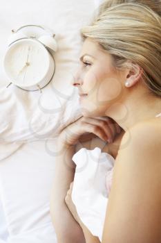 Woman Relaxing In Bed With Alarm Clock