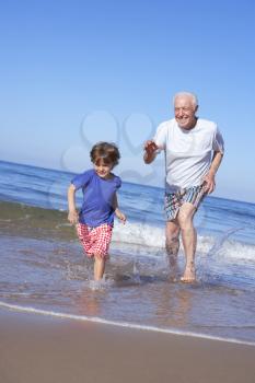 Grandfather Chasing Grandson Along Beach