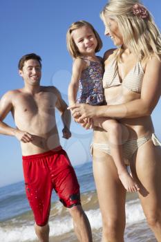 Family With Young Daughter Running Along Beach Together