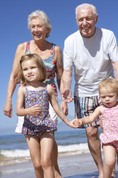Grandparents And Grandchildren Running Along Beach