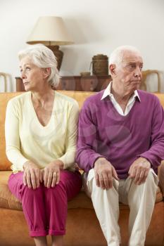 Serious Looking Senior Couple Sitting On Sofa At Home