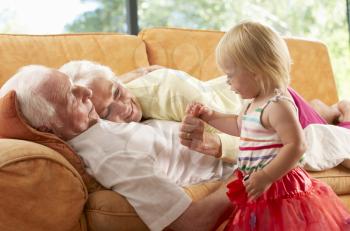 Senior Couple Lying On Sofa With Granddaughter