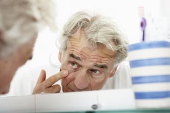 Tired Senior Man Looking At Reflection In Bathroom Mirror