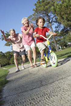 Grandparents Teaching Grandson To Ride Bike In Park