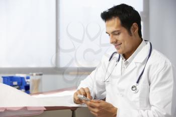 Male Doctor In Surgery Using Mobile Phone