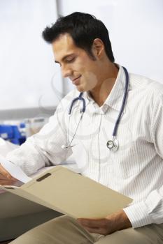 Male Doctor In Surgery Reading Patient Notes
