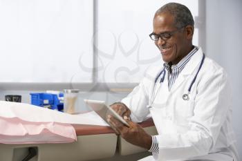 Male Doctor In Surgery Using Digital Tablet