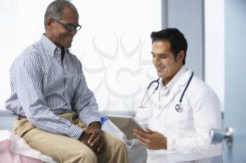 Doctor In Surgery With Male Patient Using Digital Tablet