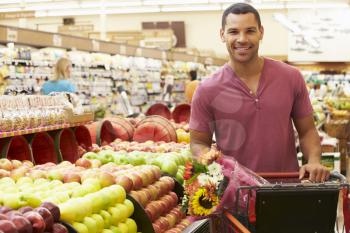 Man Pushing Trolley By Fruit Counter In Supermarket